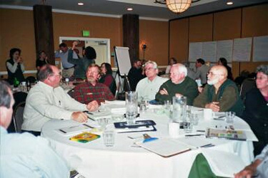 Charrette work groups work at round tables in a large meeting room-note the flip chart pages taped to the walls.