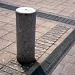 Pebbled-texture bollard mounted on bricks along a paver and brick sidewalk