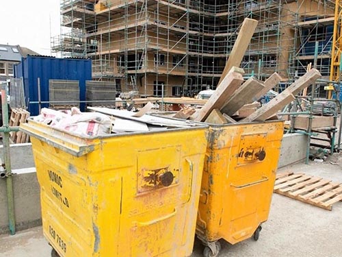 sorting construction waste into two big yellow bins on a construction site